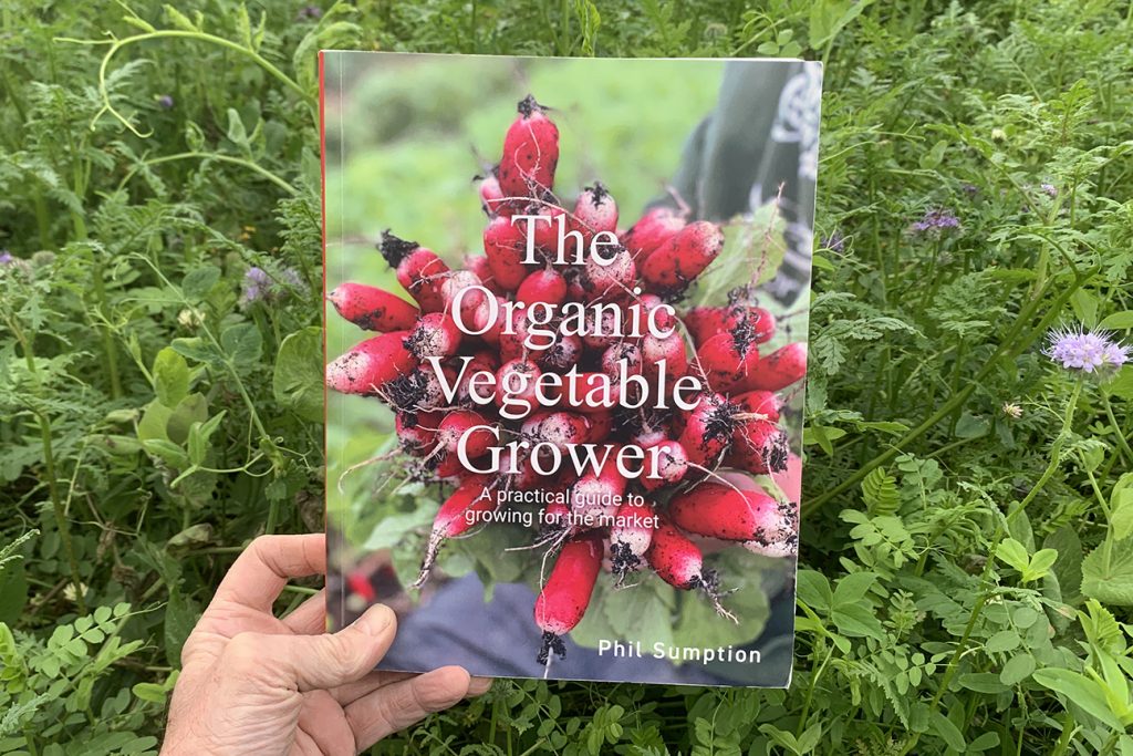 The Organic Vegetable Grower book against background of a mixed cover crop